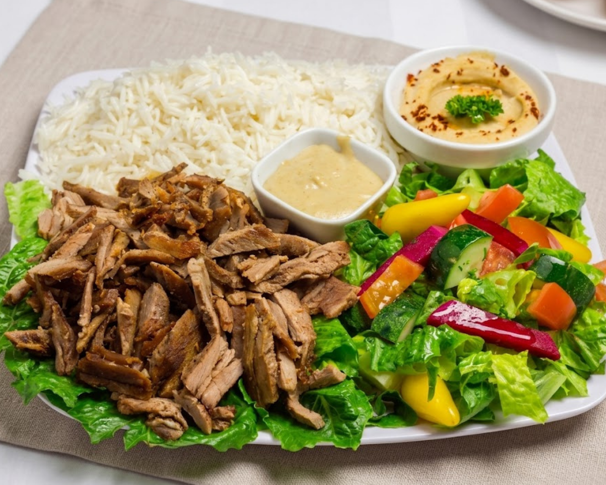 Seasoning Alley Tri-Tip Shawerma plate featuring thinly sliced, tender marinated beef tri-tip, served over seasoned rice with Mediterranean sides and tahini sauce.